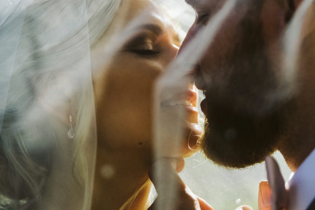 Closeup of bride and groom kissing under a veil on wedding day