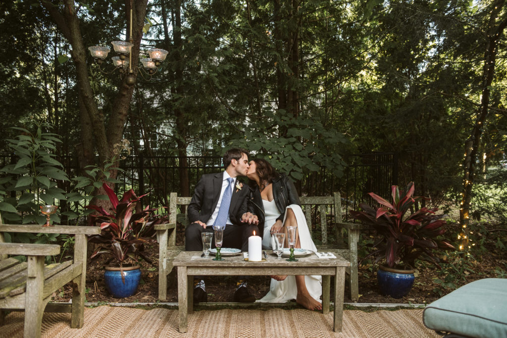 Couple kissing on a bench in a backyard wedding